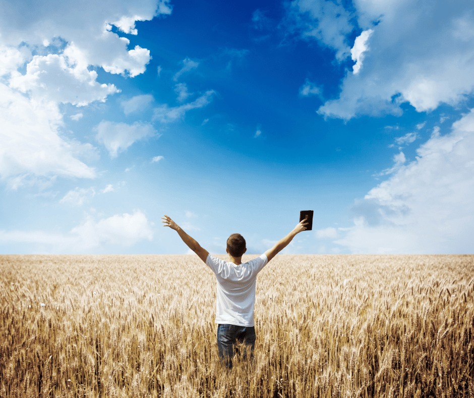 a Man in a field with his bible raising his hands in the air, praising God