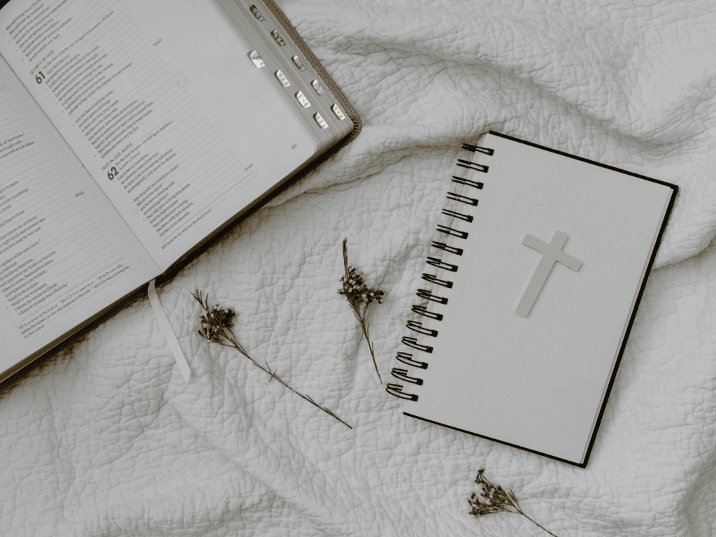 Flat lay of Bible and Christian journal with cross on white blanket – faith resources visual