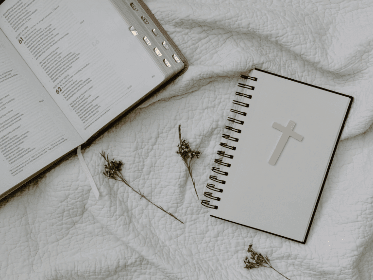 Flat lay of Bible and Christian journal with cross on white blanket – faith resources visual